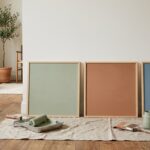 Trois panneaux de couleur sauge, argile et bleu adossés à un mur pour tester une peinture